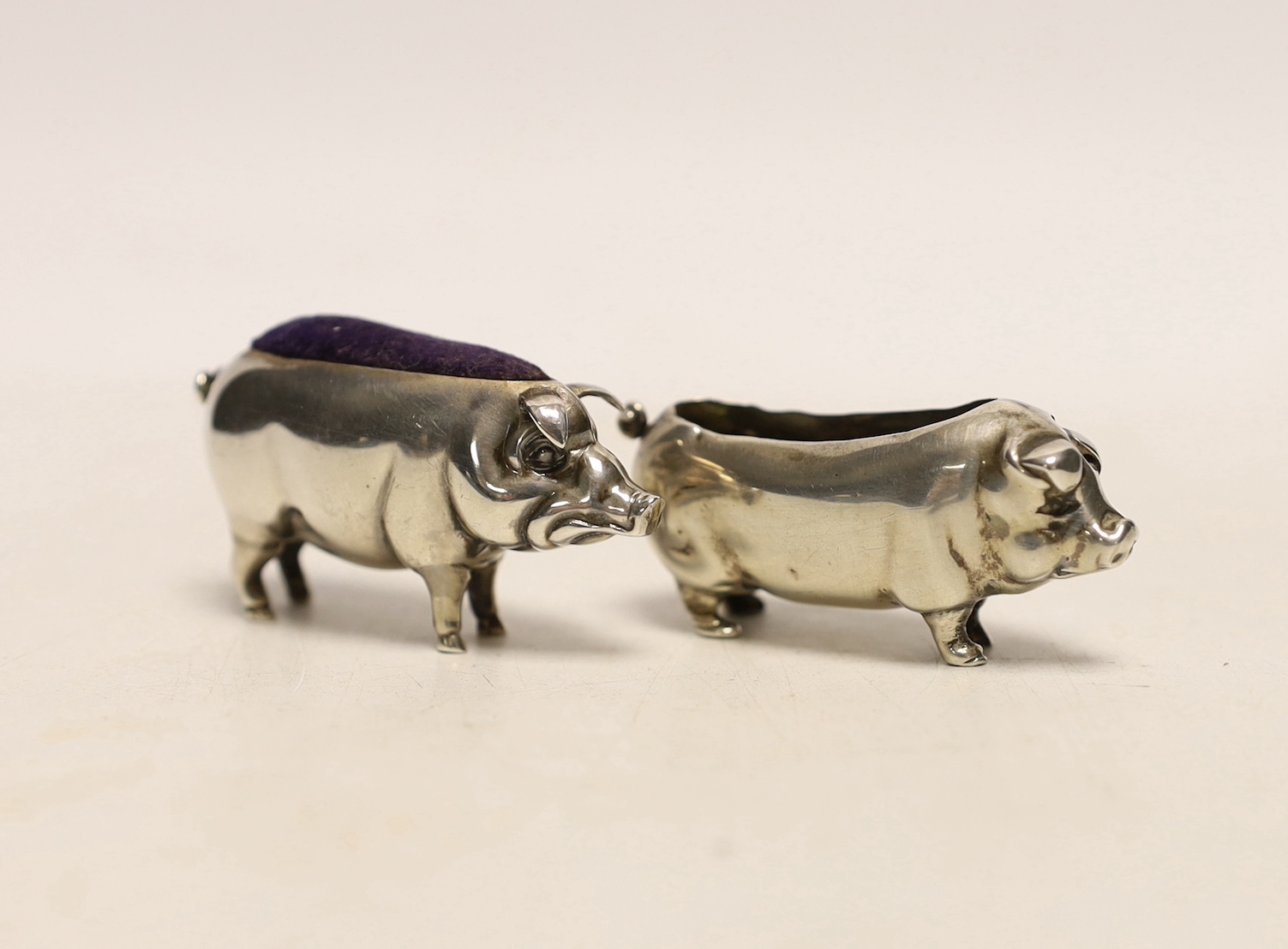 An Edwardian novelty silver pin cushion, modelled as a pig, Sydney & Co, Birmingham, 1906, length 49mm, together with one other silver pig pin cushion, marks rubbed and lacking cushion.